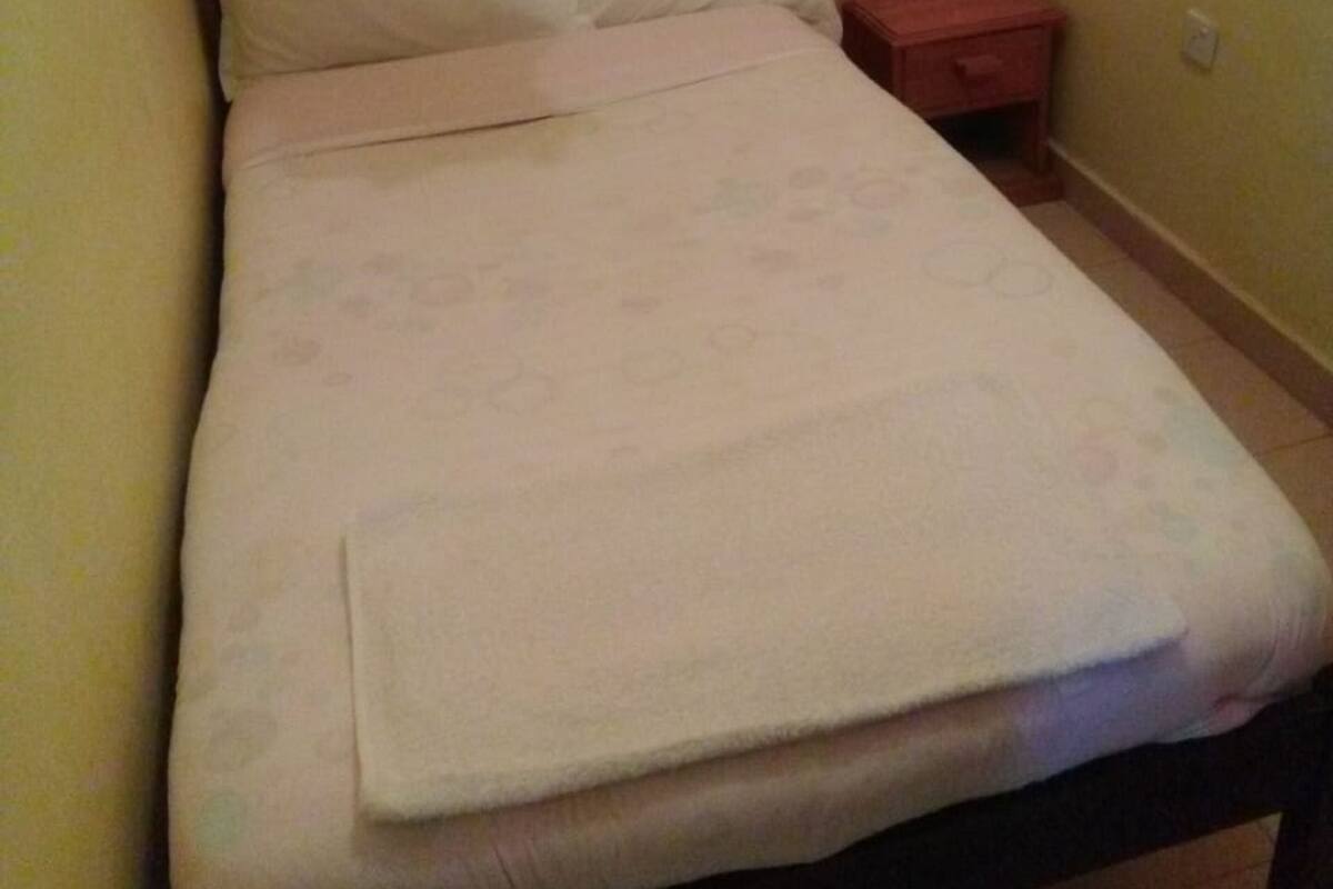 A neatly made bed with a folded blanket in a room with peach walls and a wooden nightstand.