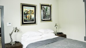 A hotel room with a bed, two bedside lamps, a nightstand, and two framed pictures on the wall.