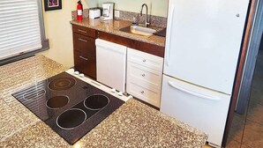 A compact kitchen with wooden cabinets, a microwave, a sink, a stove, and a refrigerator.