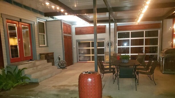 A covered patio area with a dining table and chairs, a red decorative planter, and a garage door.