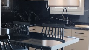 Una cocina moderna con encimera de mármol negro, sillas de madera y armarios de tonos claros.
