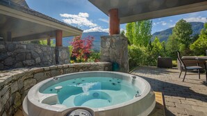 Ein Whirlpool unter einer überdachten Terrasse mit Steinmauern, einer Steinsäule und Blick auf Berge.