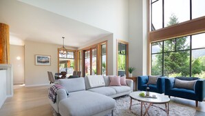 Ein geräumiges Wohnzimmer mit einer großen Eckcouch, einem blauen Sessel und einem Couchtisch. Im Hintergrund ist ein Essbereich mit Tisch und Stühlen zu sehen.