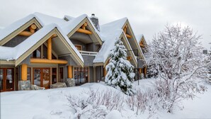 Ein mehrstöckiges Chalet mit schneebedecktem Dach und Holzbalken, umgeben von schneebedeckten Bäumen und Sträuchern.