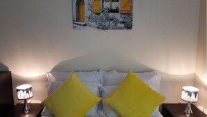 Ein Bett mit weißer Bettwäsche und zwei gelben Kissen, eingerahmt von zwei Nachttischen mit Lampen.