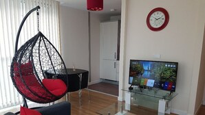 Ein modernes Wohnzimmer mit Hängesessel, Sofa, Glastisch und einem Fernseher auf einem Schrank.