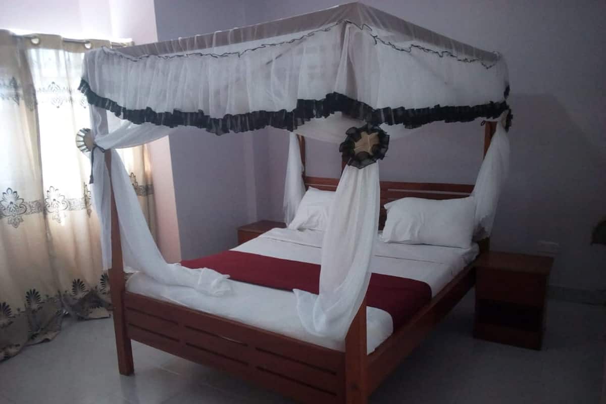 A four-poster bed with a canopy, white bedding, and a red throw blanket.