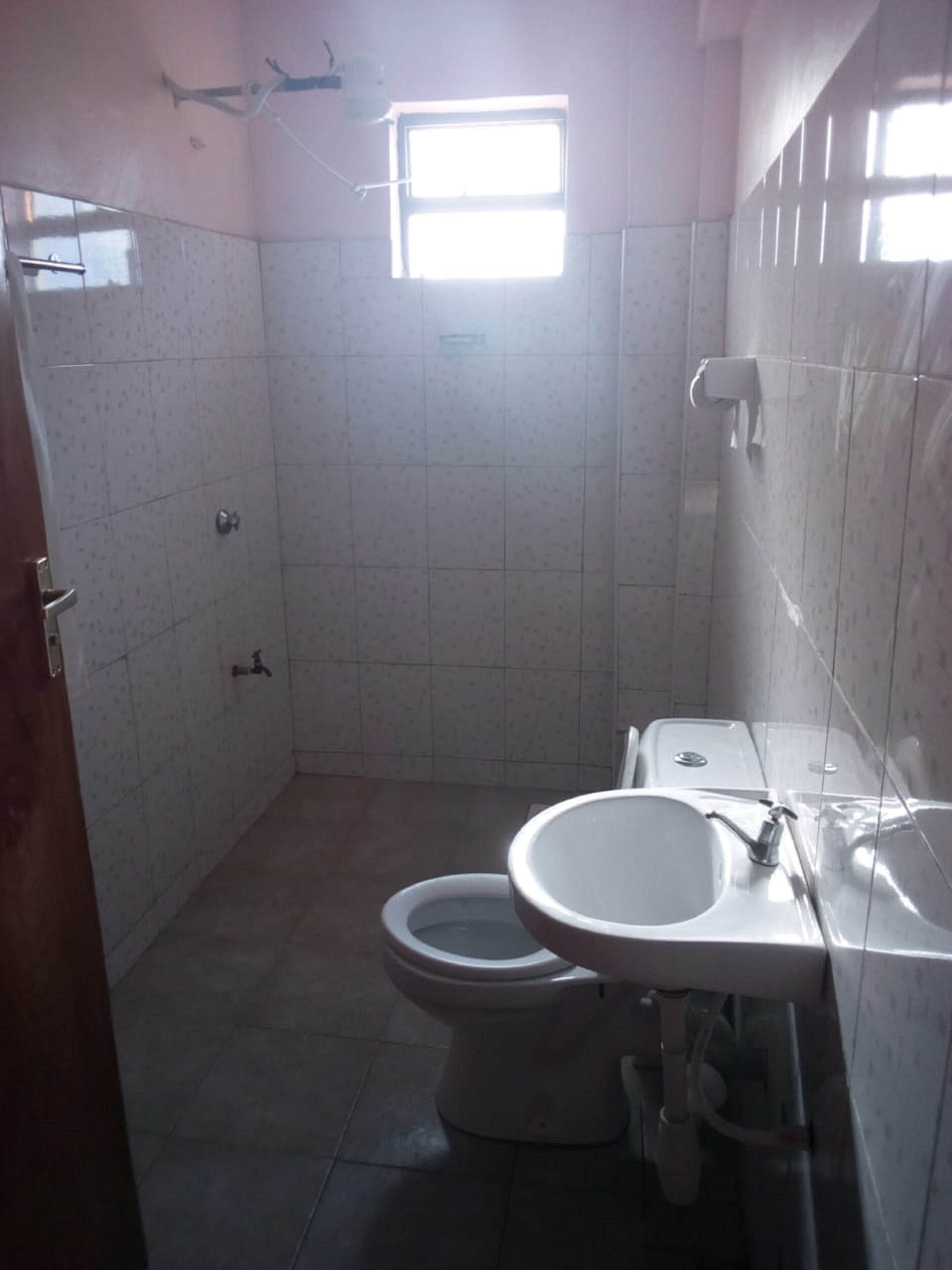 A small, tiled bathroom with a toilet, sink, and a window allowing natural light.