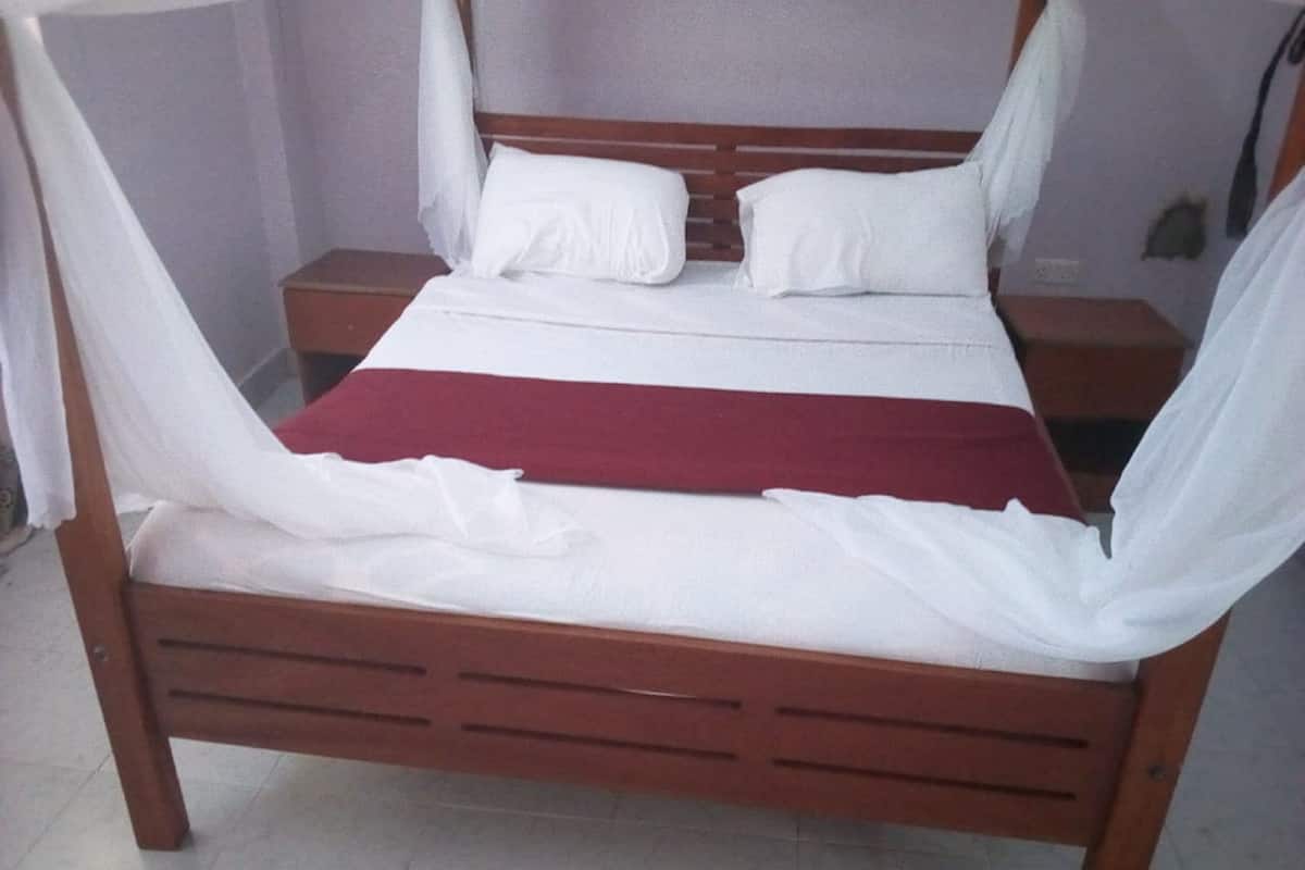 A four-poster bed with white linens and a red bedspread, wooden headboard, and nightstands with lamps.
