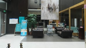 A lobby with leather sofas, a large abstract painting, a reception desk, and a potted plant. - Jinjiang Inn(Beijing Tongzhou Beiyuan Subway Station) (Tongzhou)