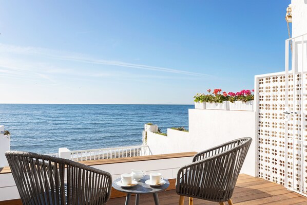 Un balcon avec deux fauteuils en osier, une petite table ronde avec des tasses, et une vue sur la mer.