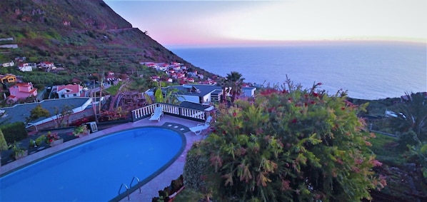 A coastal resort with a swimming pool, lounge chairs, and a view of the ocean.