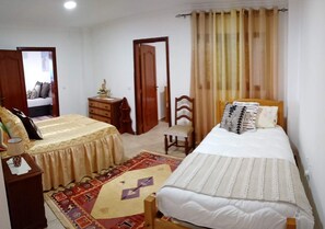 A bedroom with two beds, a wooden dresser, a chair, and a patterned rug.