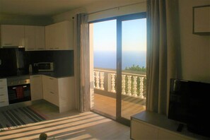 A modern kitchen with white cabinets, a microwave, and a stove. There is a sliding glass door leading to a balcony with a view of the sea.