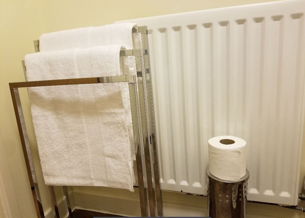 A bathroom with a towel rack holding two white towels, a toilet paper holder with a roll, and a white radiator.