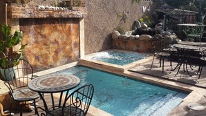 A pool area with a stone wall, a small waterfall, and outdoor seating. - One32 Guest House (Kingston)