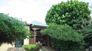A house with a stone staircase leading to a wooden door, surrounded by lush greenery and a car parked nearby. - One32 Guest House (Kingston)