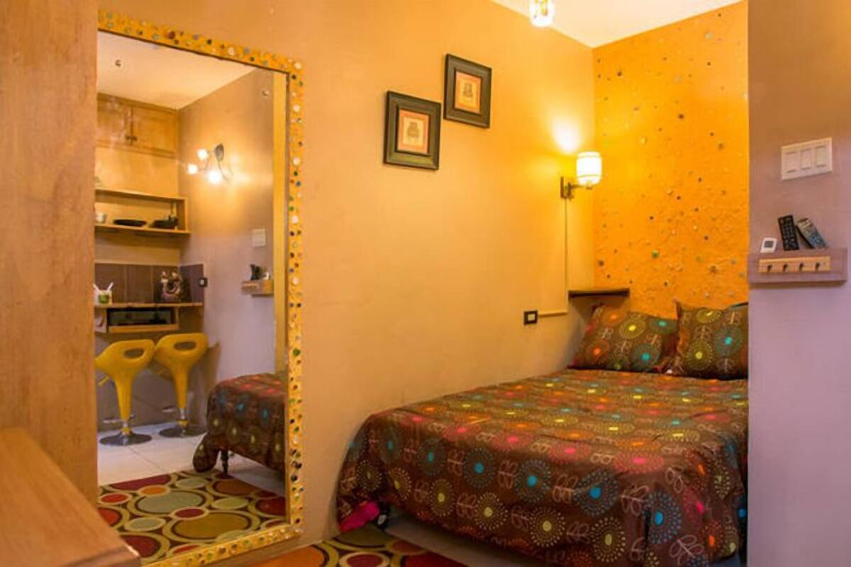 Un dormitorio con una cama, un espejo, una lámpara fijada a la pared y un estante con objetos.