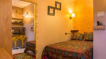 Quarto com cama, espelho, luminária na parede e uma pequena prateleira com objetos.