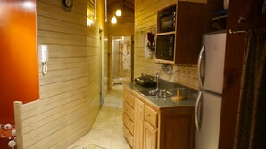 A narrow kitchen with wooden cabinets, a refrigerator, a microwave, and a sink. - One32 Guest House (Kingston)