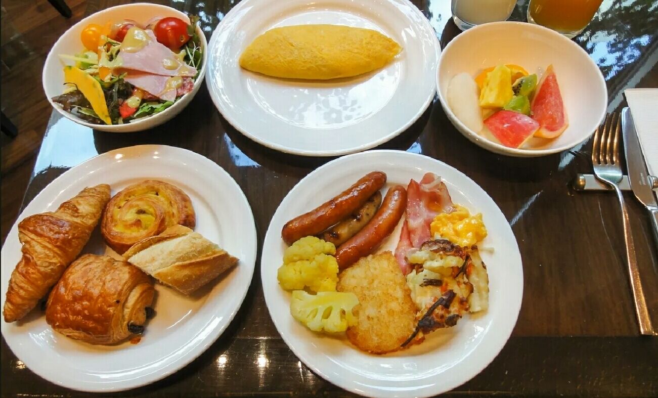 A breakfast table with plates of croissants, sausages, and a salad.