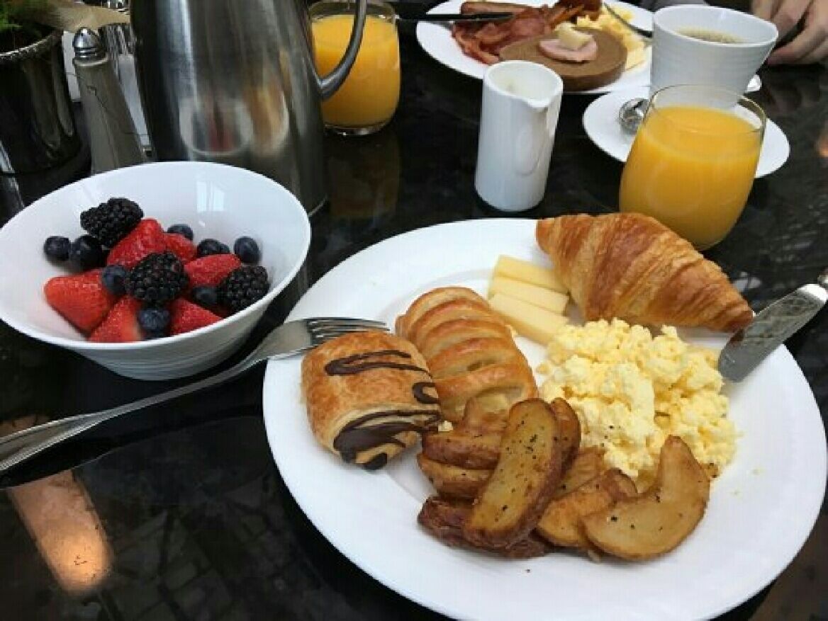 Une table dressée pour le petit-déjeuner avec une assiette d’œufs, des pommes de terre, un croissant et un bol de fruits rouges.