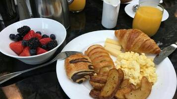 Une table dressée pour le petit-déjeuner avec une assiette d’œufs, des pommes de terre, un croissant et un bol de fruits rouges.