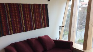 A room with a wooden ceiling, a maroon sofa, a small wooden table, and a woven basket. - Single gîte heliodome (Ostwald)