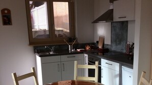 A kitchen with a round wooden table and four chairs, a window with blinds, and a stove. - Single gîte heliodome (Ostwald)