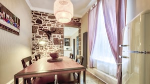 Un comedor con mesa de madera, sillas, pared de piedra, candelabro y refrigerador.