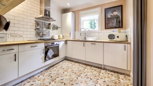 Una cocina moderna con armarios blancos, piso estampado y ventana con vista a follaje.
