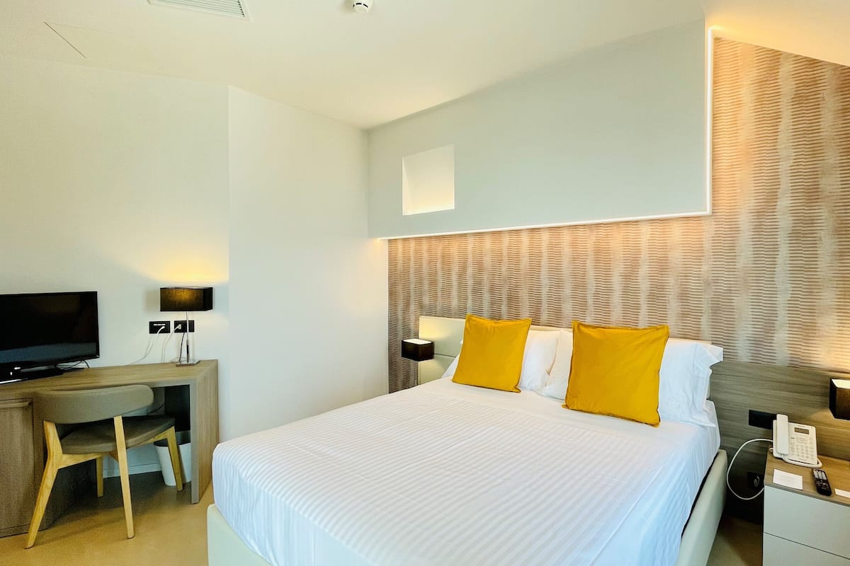 Een hotelkamer met een bed, een bureau, een televisie, een telefoon en een wandlamp.