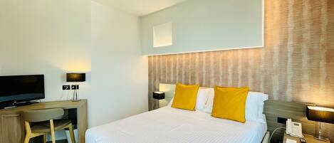A hotel room with a bed, a desk, a television, a phone, and a wall-mounted light.