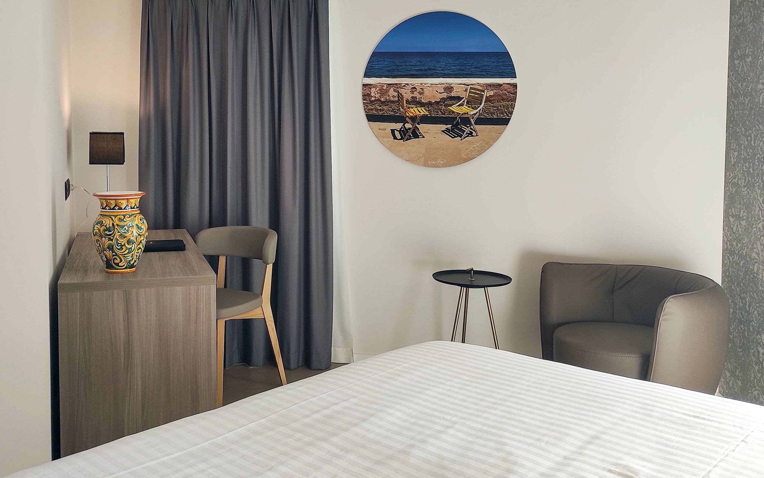 Habitación de hotel con cama, escritorio, silla, una mesita y un cuadro de playa.