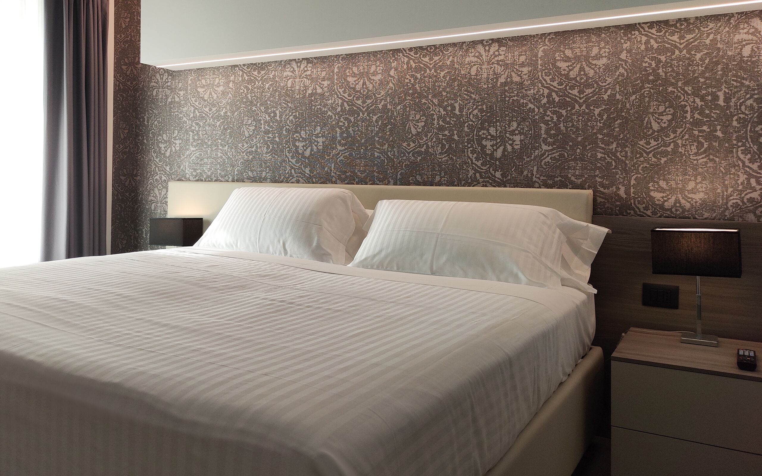 A neatly made bed with white linens, a headboard, and two bedside lamps on a nightstand.