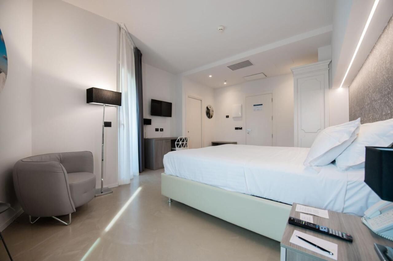 Quarto de hotel moderno com uma cama grande, uma escrivaninha com cadeira, um abajur e uma televisão de tela plana.