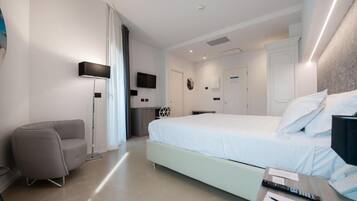 Quarto de hotel moderno com uma cama grande, uma escrivaninha com cadeira, um abajur e uma televisão de tela plana.