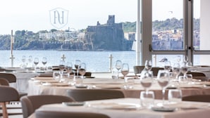 Un restaurante con mesas preparadas para comer, con vista a una ciudad costera y un castillo histórico.