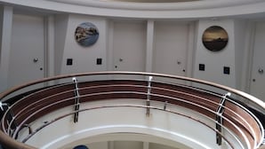 Una escalera curva con barandas metálicas y vistas de los muros interiores con obras de arte y números de puerta.