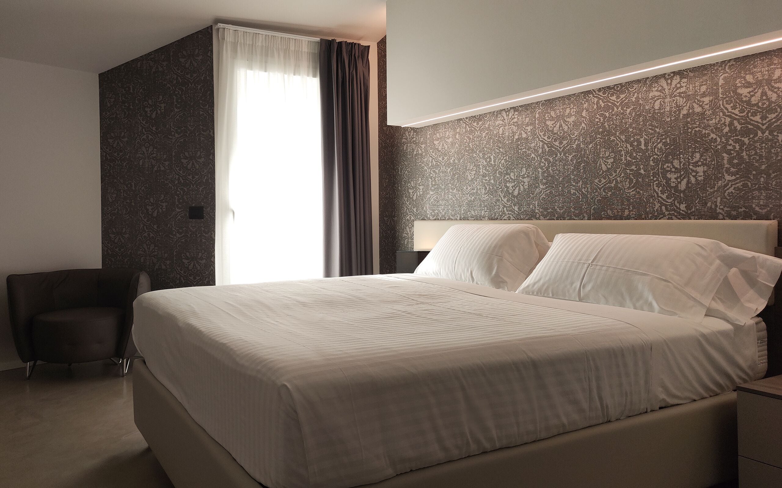 A hotel room with a large bed, a chair, and a nightstand.