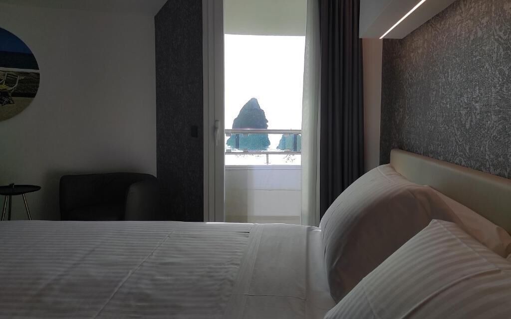 Une chambre d’hôtel avec un lit, une chaise, une table ronde et une vue sur un balcon avec une montagne en arrière-plan.
