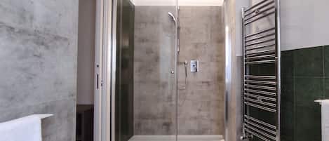 A glass-enclosed shower with a handheld showerhead and a wall-mounted faucet.