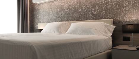 Quarto de hotel moderno com uma cama grande, uma mesa de cabeceira com abajur e papel de parede estampado.