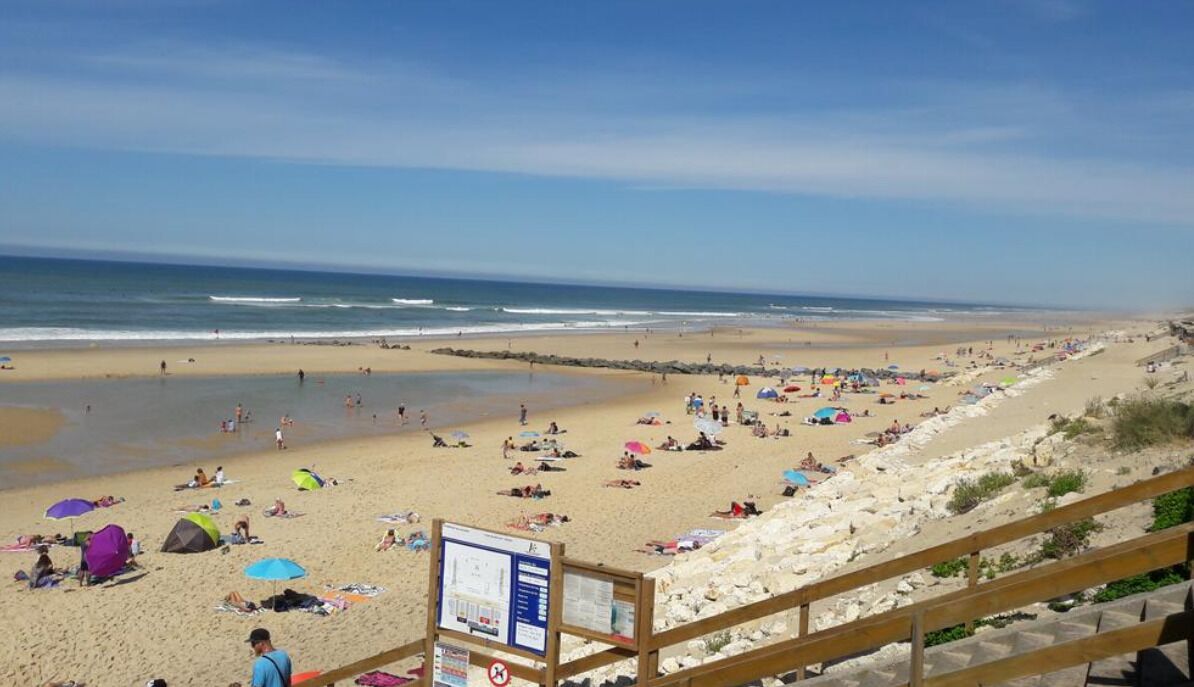 A beach with people sunbathing and swimming, a wooden boardwalk, and a lifeguard stand.
