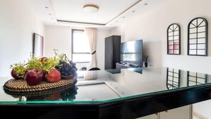 A modern kitchen with a glass countertop, a central island with a fruit bowl, a built-in oven, and a large window with curtains. - Tranquil King David Apartment with Free Parking (Jerusalem)