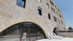 A stone building with large arched windows and a balcony area with lounge chairs. - Tranquil King David Apartment with Free Parking (Jerusalem)