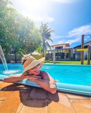 A person relaxing by a pool with a clear view of a building and palm trees in the background. - Pousada Trilha do Mar (Marechal Deodoro)