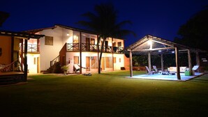 A two-story house with a covered outdoor seating area and a well-lit entrance. - Pousada Trilha do Mar (Marechal Deodoro)