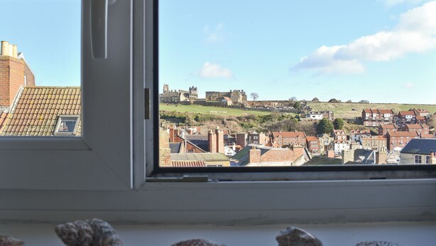 Une vue depuis une fenêtre sur une ville avec des bâtiments historiques et une colline en arrière-plan.