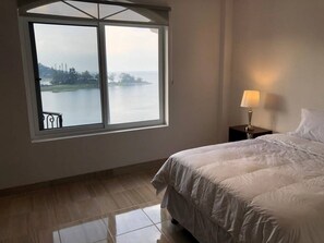 A bedroom with a large window, a bed, a nightstand, and a lamp. - CasaDePiedra, CerroDeOro, LagoAtitlan, Brand New (Sector Tzanguacal)